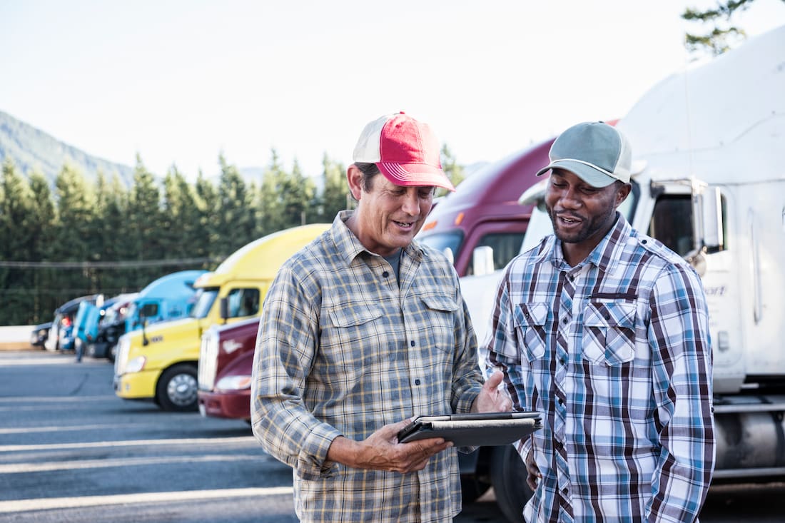 Two truck drivers discussing logistics with a tablet.